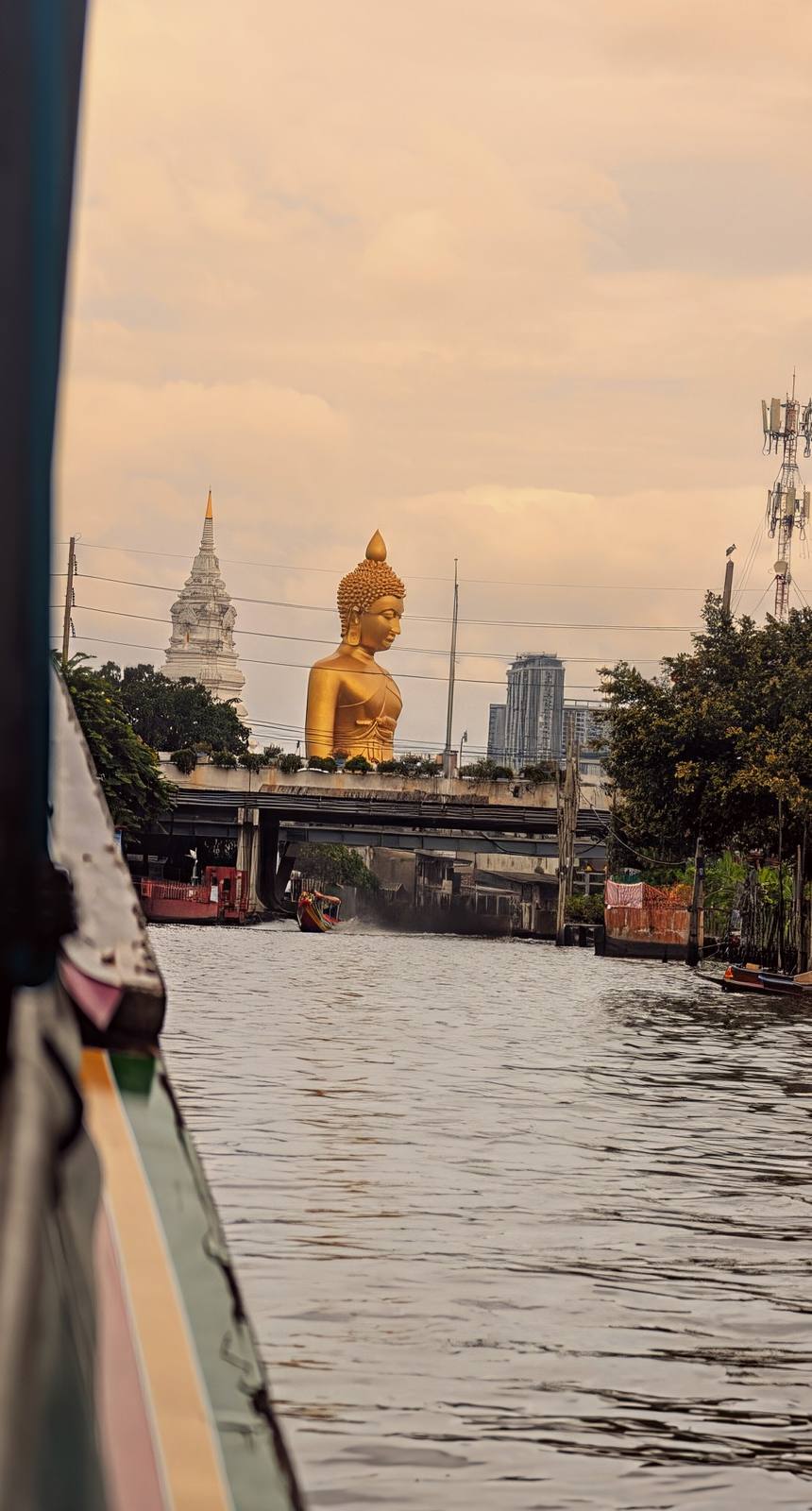 Barca de cola larga navegando por un canal de Thonburi en Bangkok, con un Buda dorado y una pagoda blanca al fondo