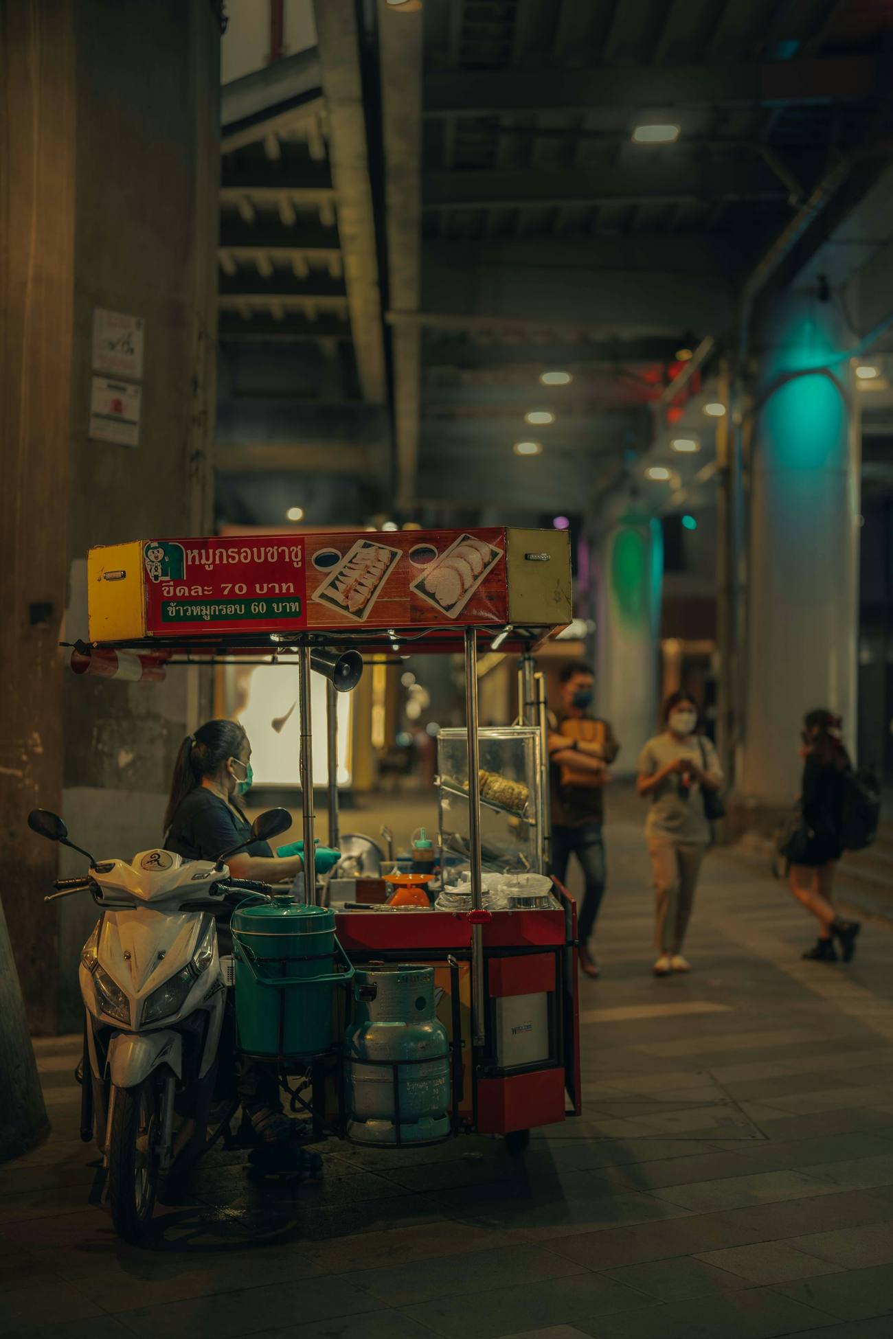 Puesto de comida callejera nocturno en Bangkok con cerdo asado y arroz, con los precios en baht