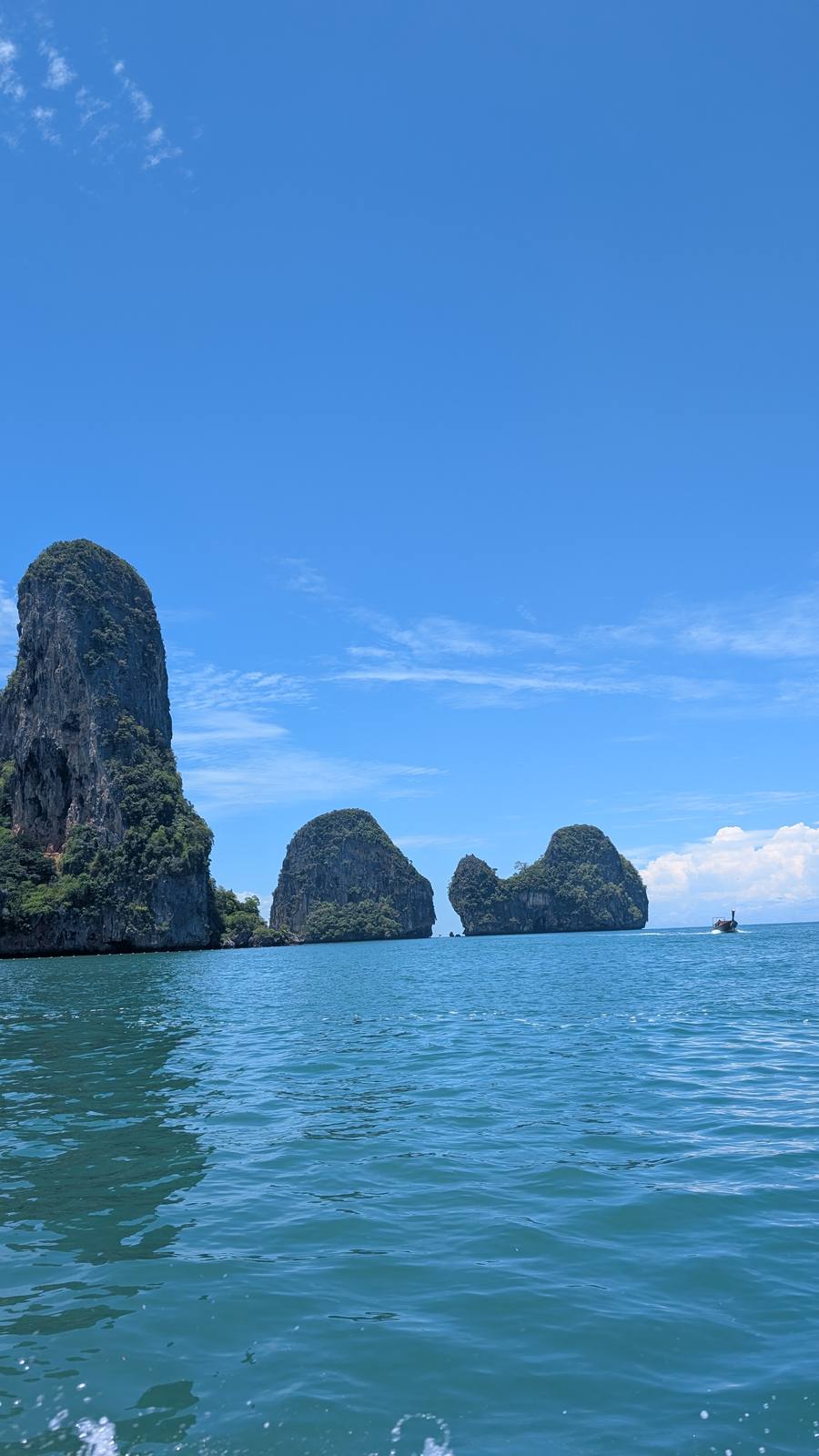 Torres de roca caliza emergiendo del mar turquesa de Krabi, con una barca longtail navegando cerca