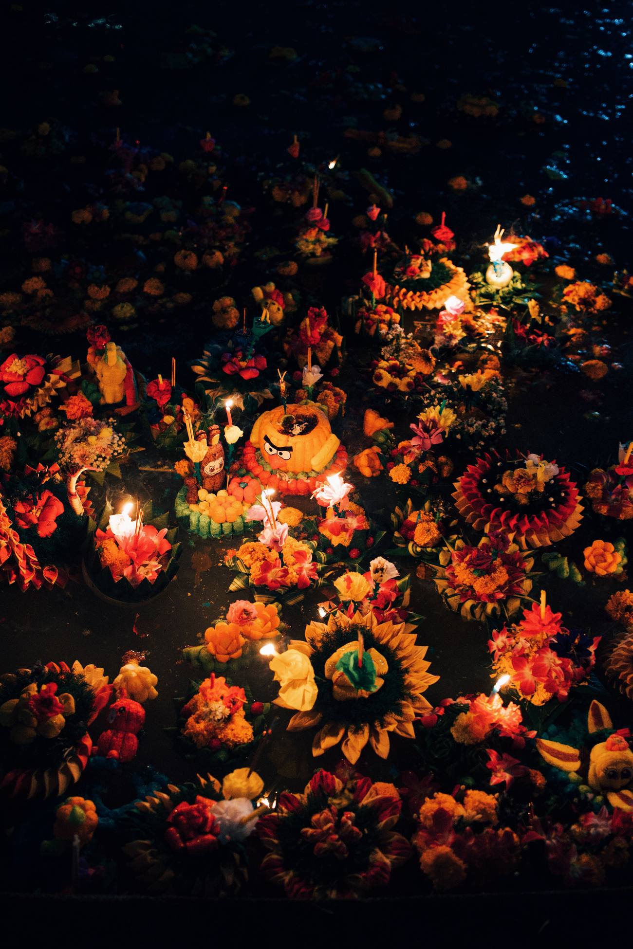Krathongs decorados con flores y velas encendidas flotando de noche sobre el agua durante el festival de Loy Krathong