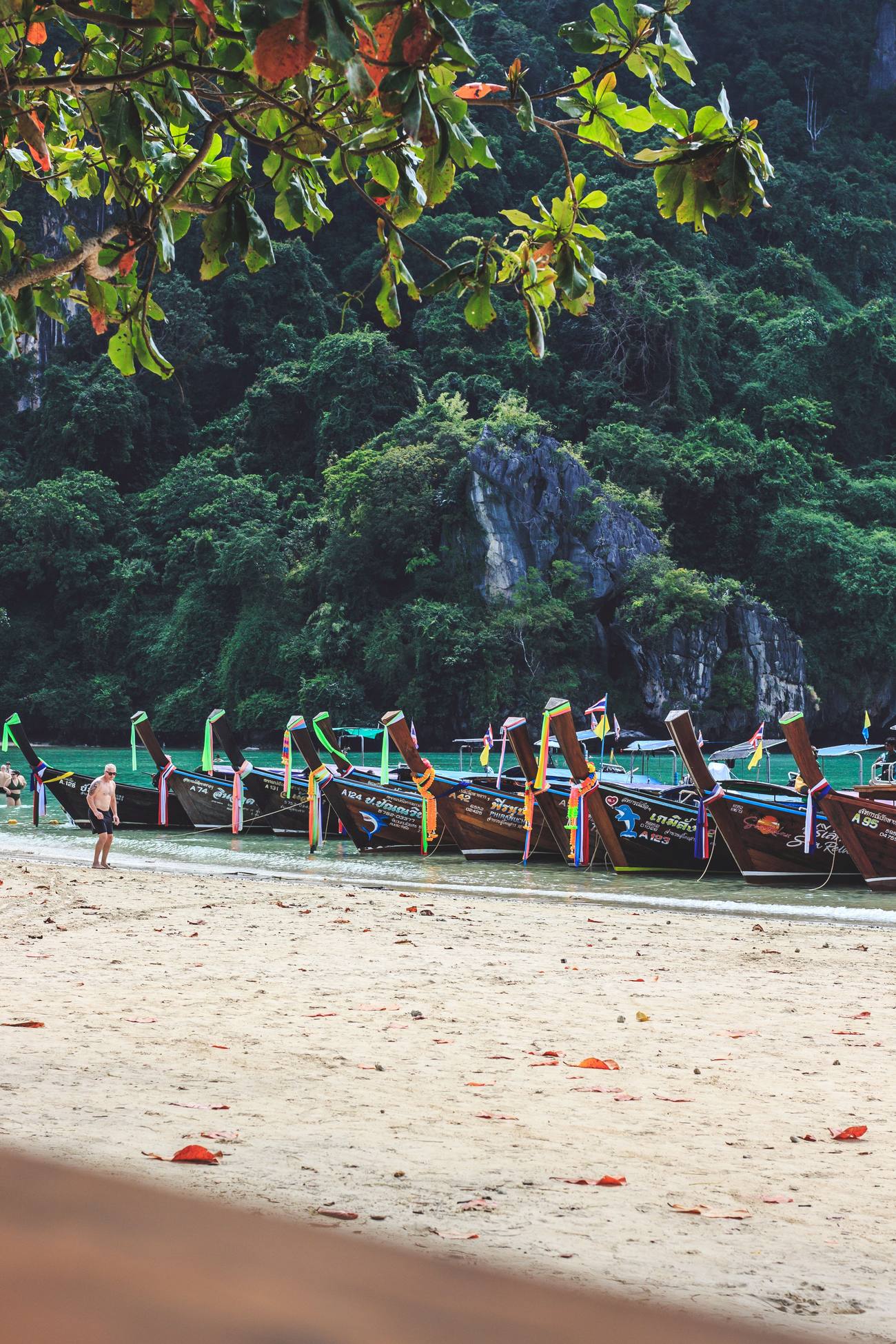 Viajero paseando solo por una playa de Tailandia junto a barcas de pescadores